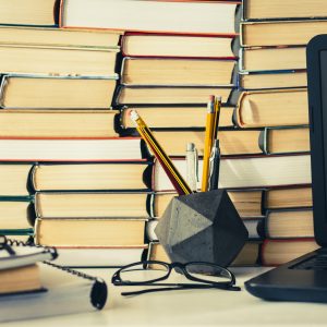 Stack of books, notebook, laptop, glasses in office background for education learning concept